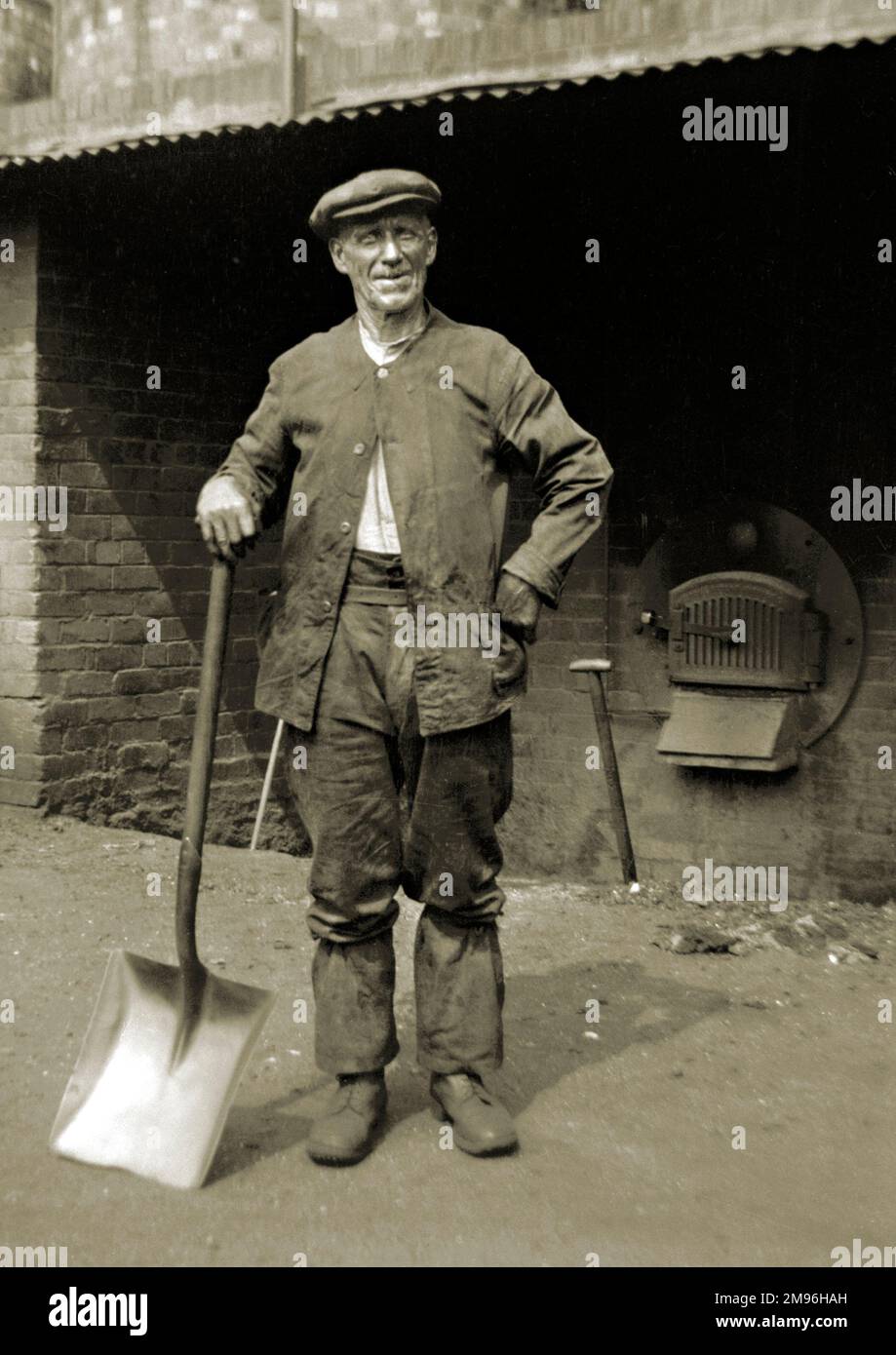 Ein Arbeiter mittleren Alters, der in einem Hof mit einem großen Spaten steht. Stockfoto