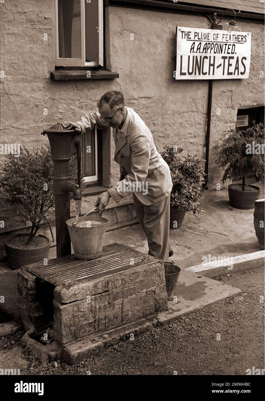 Ein Mann, der an einer Wasserpumpe einen Eimer füllt, vor einem Gasthaus namens „The Plume of Feathers“, empfohlen von der Automobilvereinigung, serviert Mittagessen, Tee und Apfelwein vom Fass. Stockfoto
