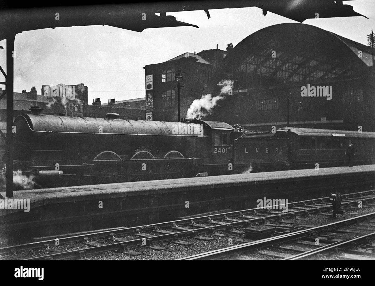 Eine LNER (London & North Eastern) Dampflok (mit dem Namen City of Kingston upon Hull) mit Tender und Kutschen auf einer Eisenbahnstrecke direkt vor einem Bahnhof. Stockfoto