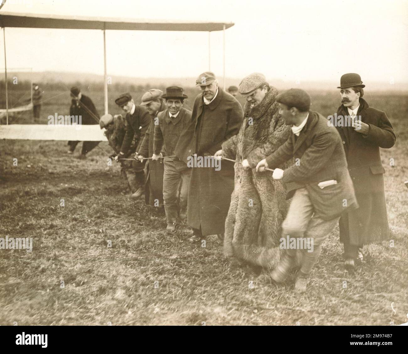 Lord Northcliffe (im Pelzmantel) hilft beim Transport der Wright A in Pau, 1909. Der ehemalige konservative Premierminister Arthur Balfour steht links von Lord Northcliffe. Orville Wright befindet sich auf der rechten Seite. Stockfoto