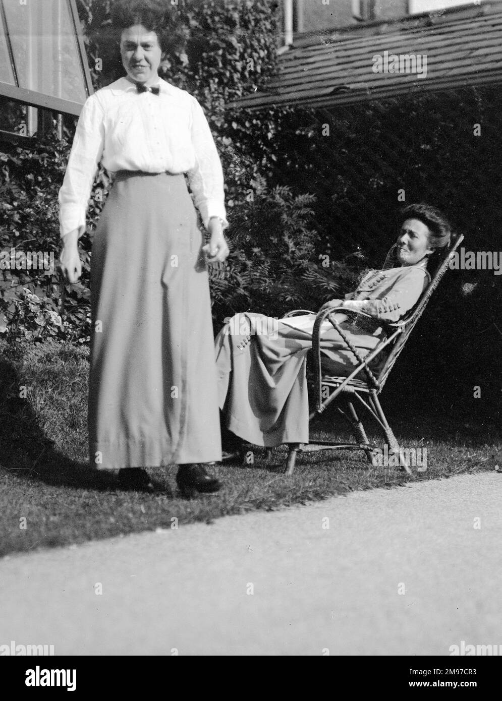 Zwei edwardianische Frauen im Garten von Strathclyde, Offerton Lane, Stockport. Steht Edith Battersby, die von ihrer Geburt im Jahr 1884 bis zum Verkauf des Hauses um 1932 dort lebte. Auf dem Tisch sitzt Kate Nash, eine Freundin der Familie aus Essex und häufige Besucher. Stockfoto
