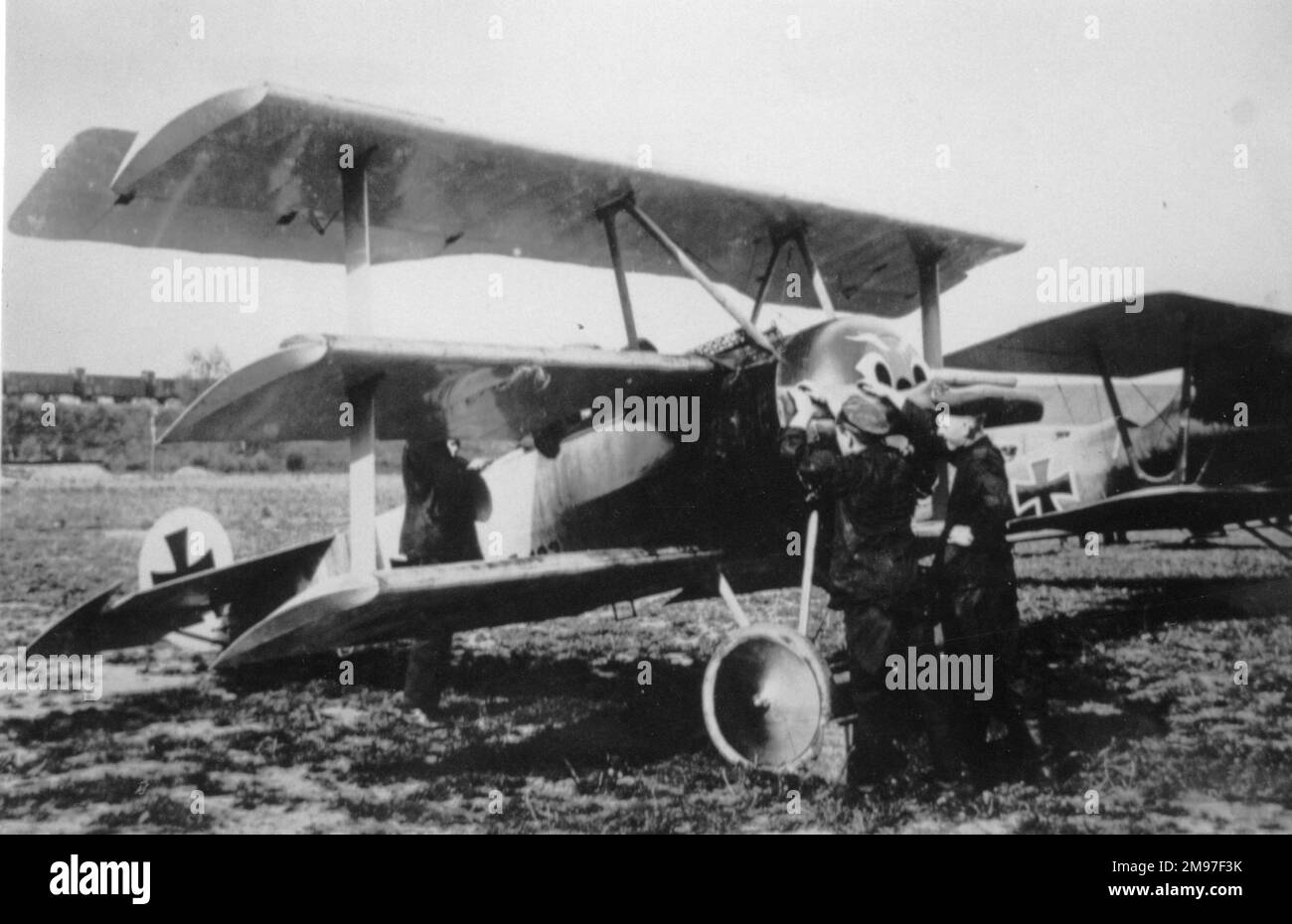 Fokker Dr. I. Deutsches Kampftriflugzeug mit einem Pfalz D III im Hintergrund. Der Pilot des Fokker bereitet sich auf den Start vor, mit einem Mechaniker, der bereit ist, den Propeller zu schwenken, und zwei weiteren in Anwesenheit. Stockfoto