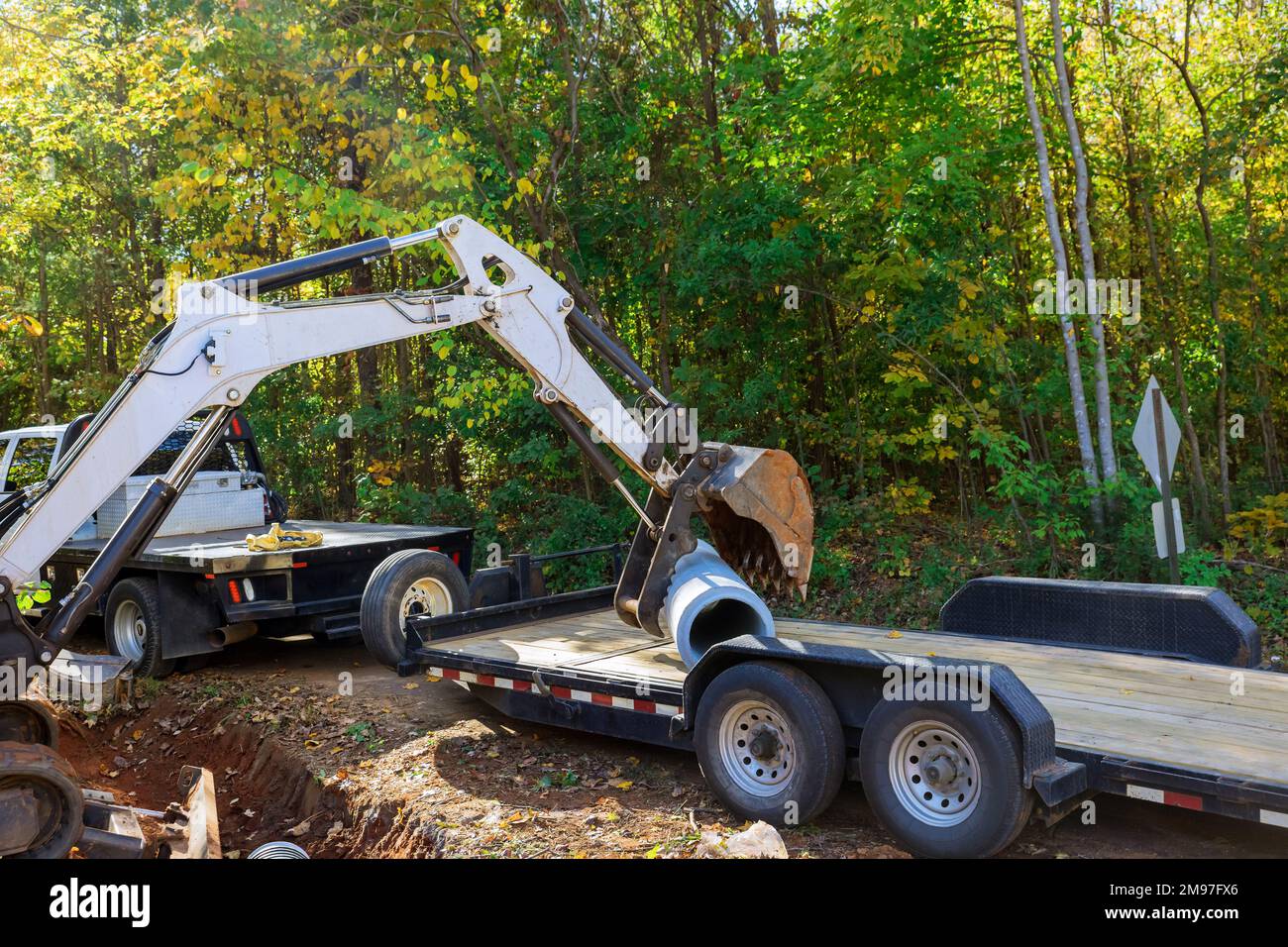 Da Betonkläranlagen für unterirdische Installationen vorbereitet werden, verwendet der Arbeiter den Traktor, um das Rohr in den Boden zu heben. Stockfoto