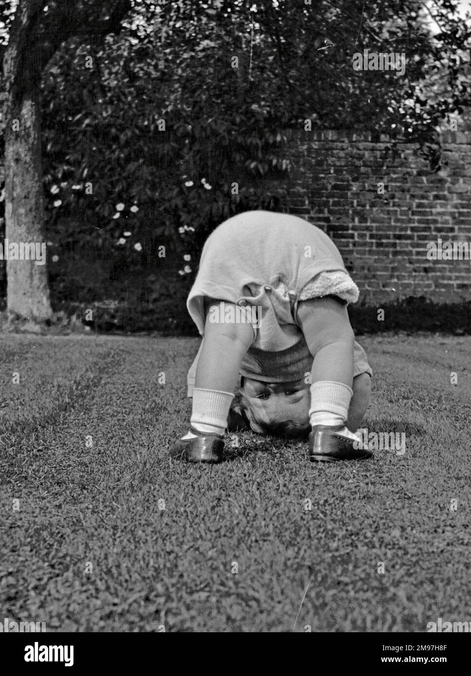 Kleinkind bückt sich in einem Garten. Stockfoto