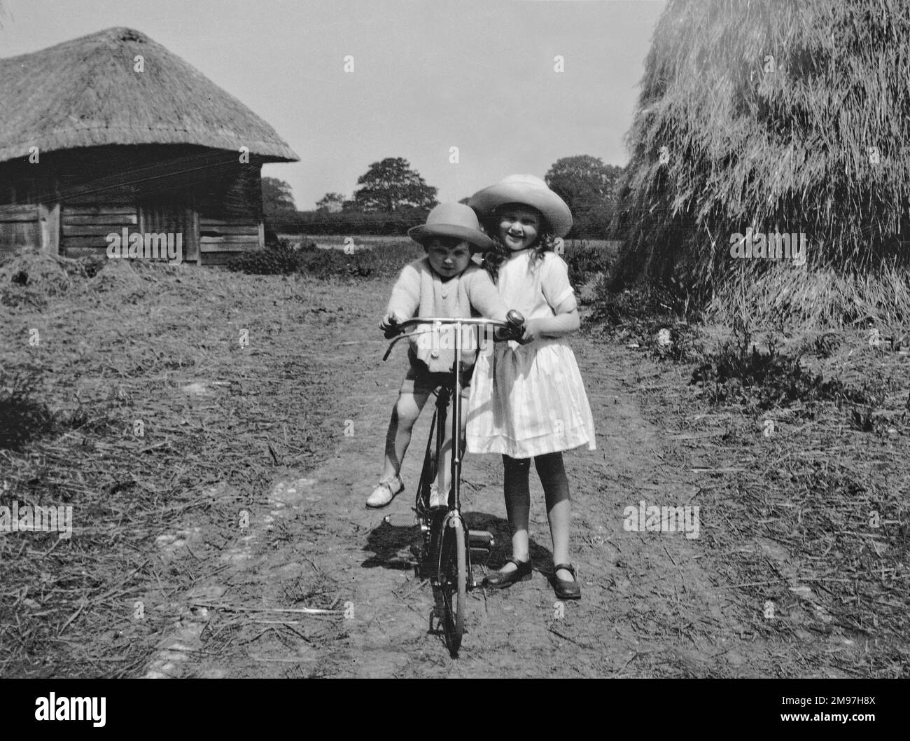 Mädchen und Kleinkind, die auf einem Feld mit dem Fahrrad fahren. Stockfoto