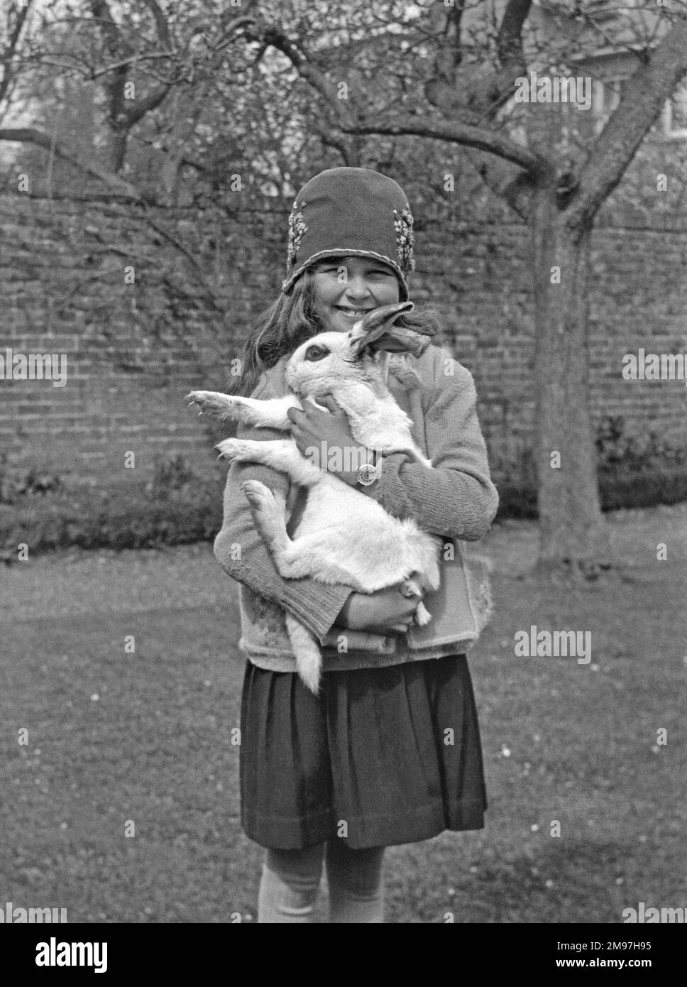 Ein lächelndes Mädchen, das sein Kaninchen in einem Garten hält. Stockfoto