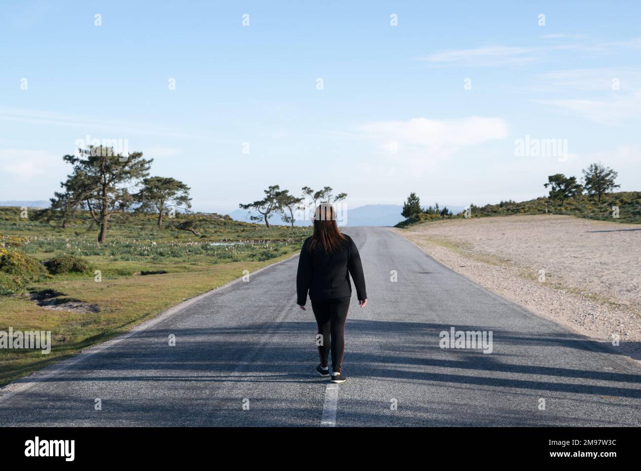 Rückansicht einer Frau, die mitten auf der Straße entlang geht, Galicien, Spanien Stockfoto