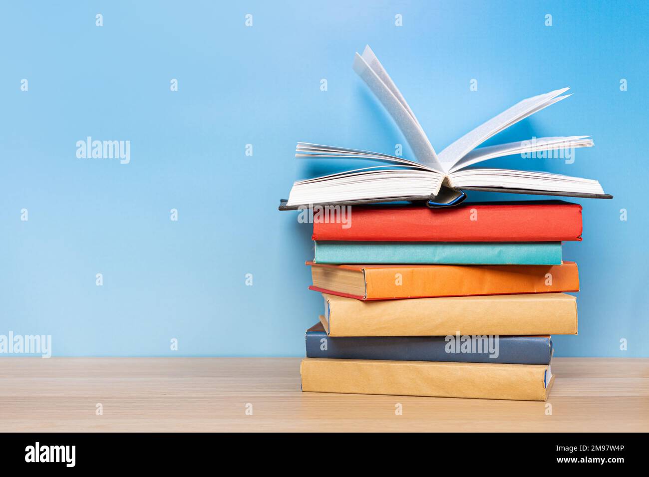 Der Stapel Bücher auf dem farbigen Einband lag und öffnete das Buch mit alten Seiten auf dem Holztisch und blauem Hintergrund. Lernkonzept im Bildungsbereich Stockfoto