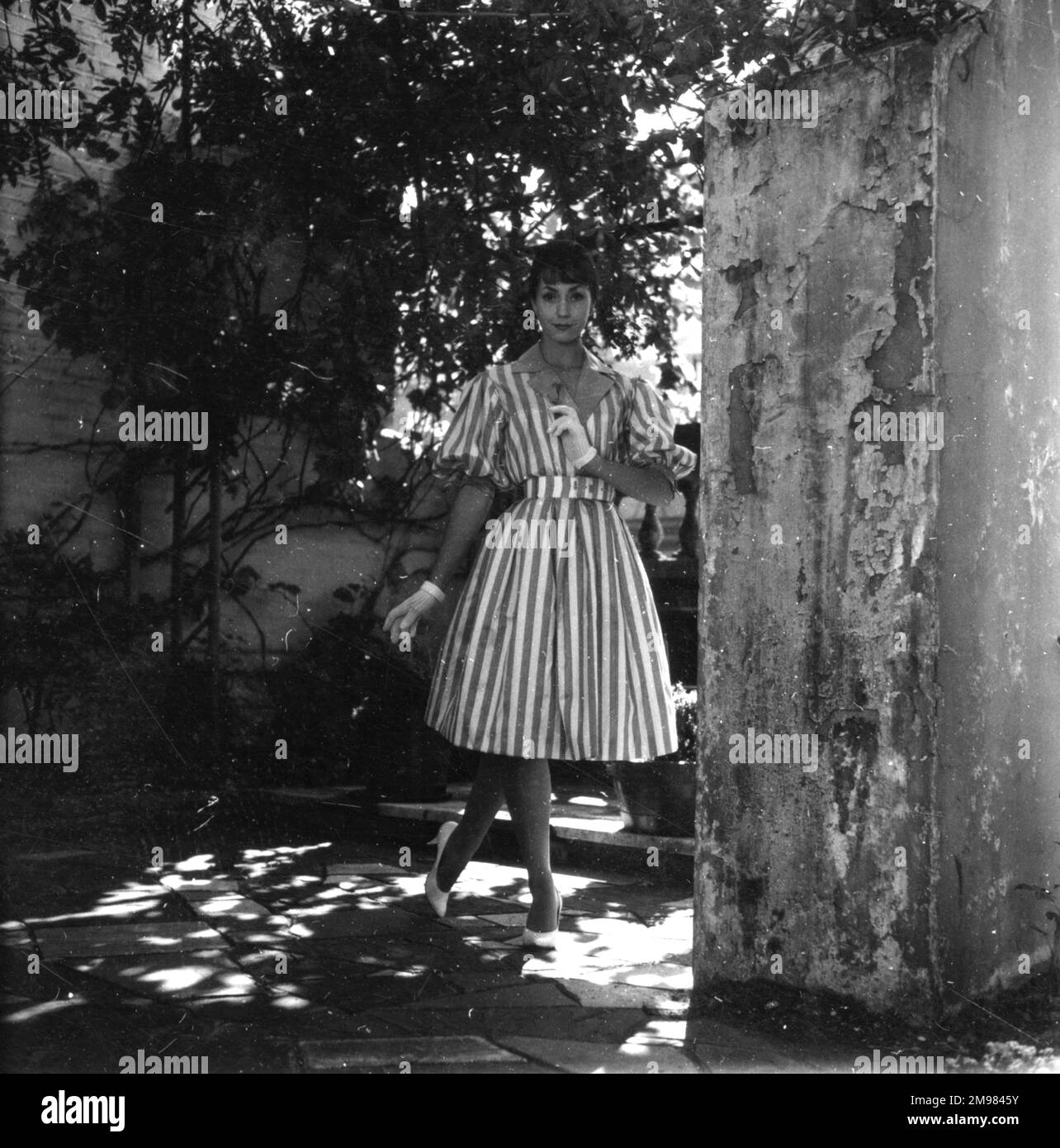 Junge Frau (Model - Geraldine Hill), die ein Kleid in einem Garten vorführt. Stockfoto