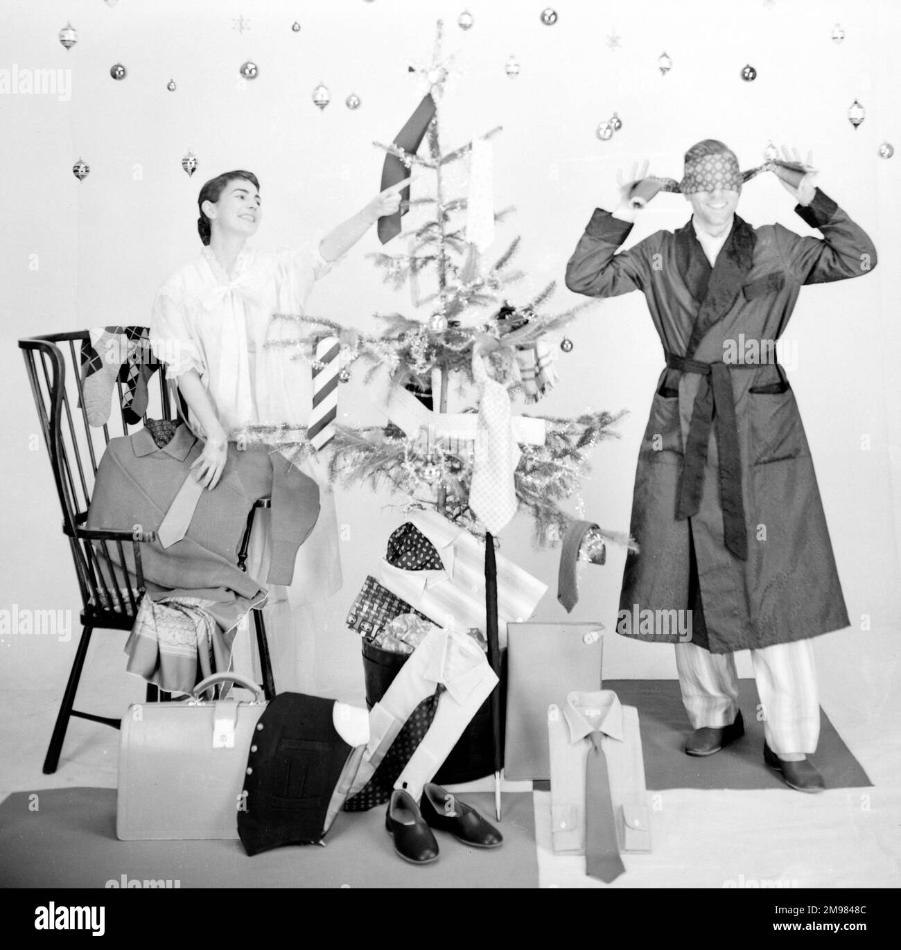 Männliche und weibliche Models in einer Weihnachtsmorgenszene mit Baum und Geschenken. Stockfoto
