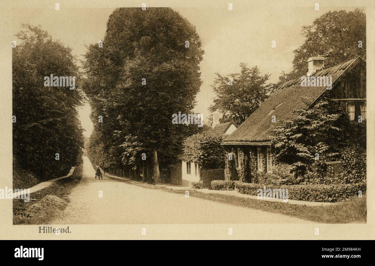 In der Ferne Rollen Pferde und Wagen eine ruhige, von Bäumen gesäumte Straße in der dänischen Stadt Hillerod hinauf. Stockfoto
