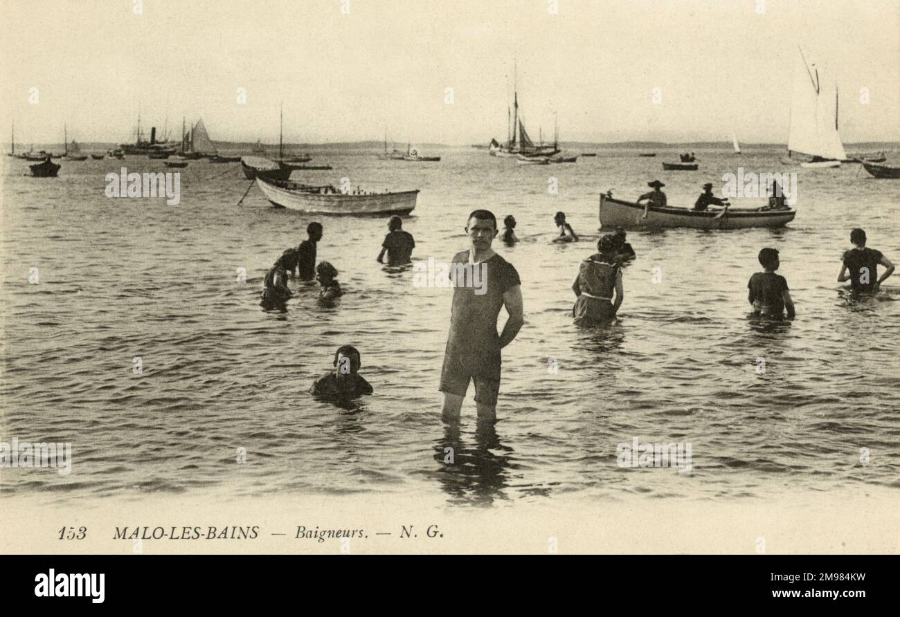 Ein Mann im Badeanzug steht in der Brandung des Strands Malo-les-Bains, nahe Dünkirchen in Frankreich. Hinter ihm sind andere Badende und verschiedene Boote. Stockfoto