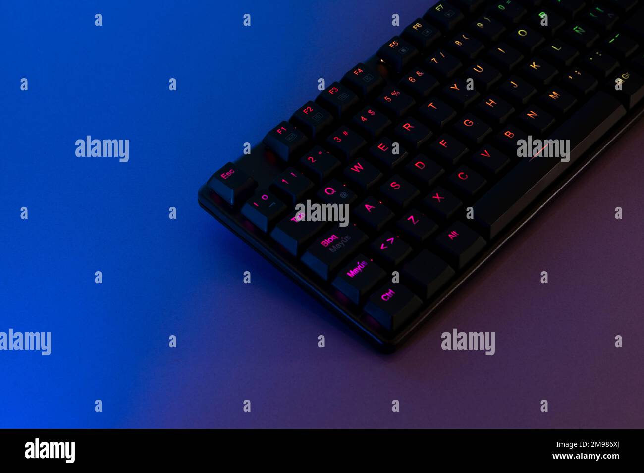 rgb-beleuchtete Spieletastatur auf einem Schreibtisch mit blauer und lilafarbener Beleuchtung. Stockfoto