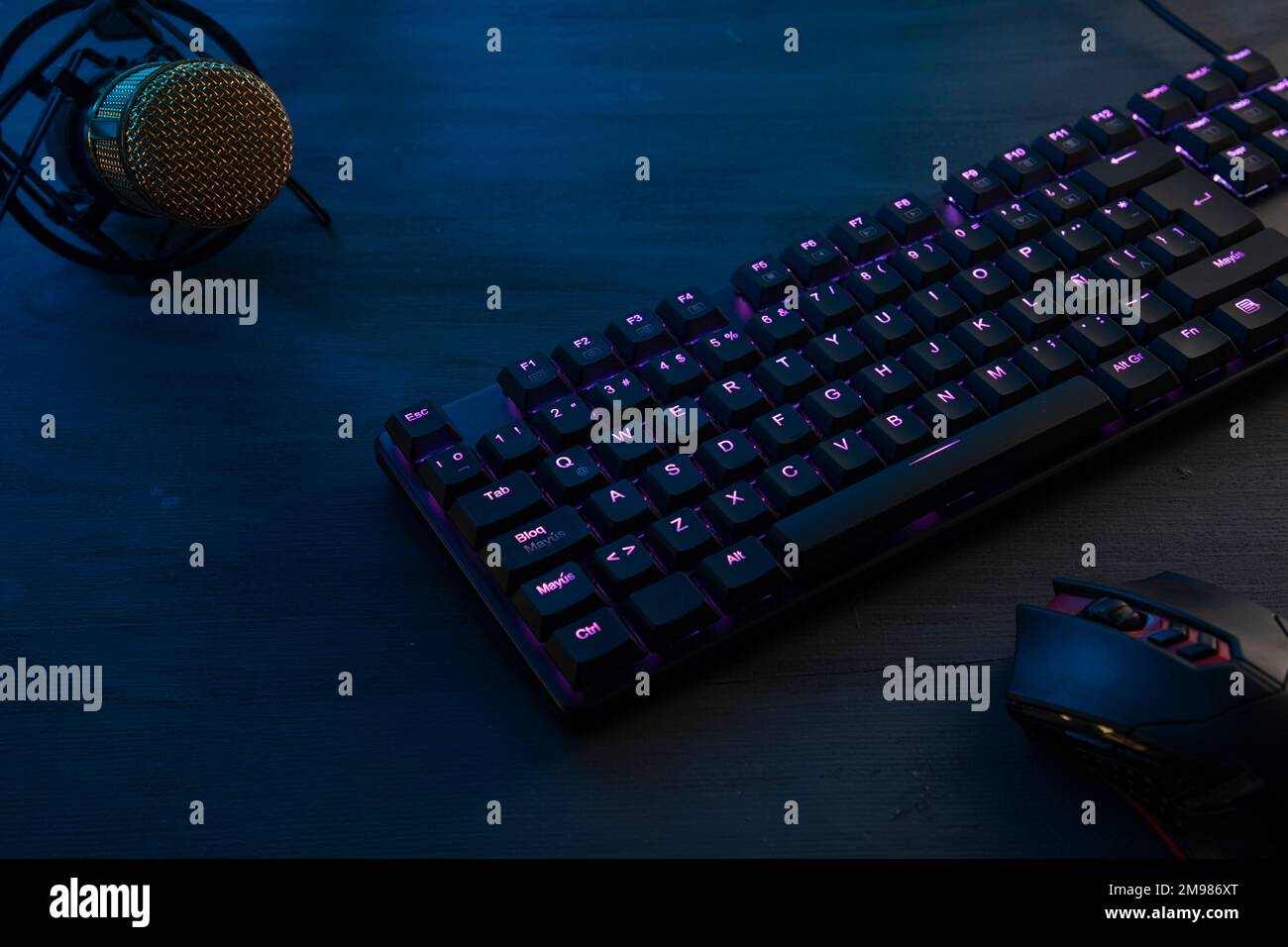 Schwarzer Holzschreibtisch mit Gamer-Tastatur, Maus und Mikrofon, die während des Online-Spielens übertragen werden können. Stockfoto