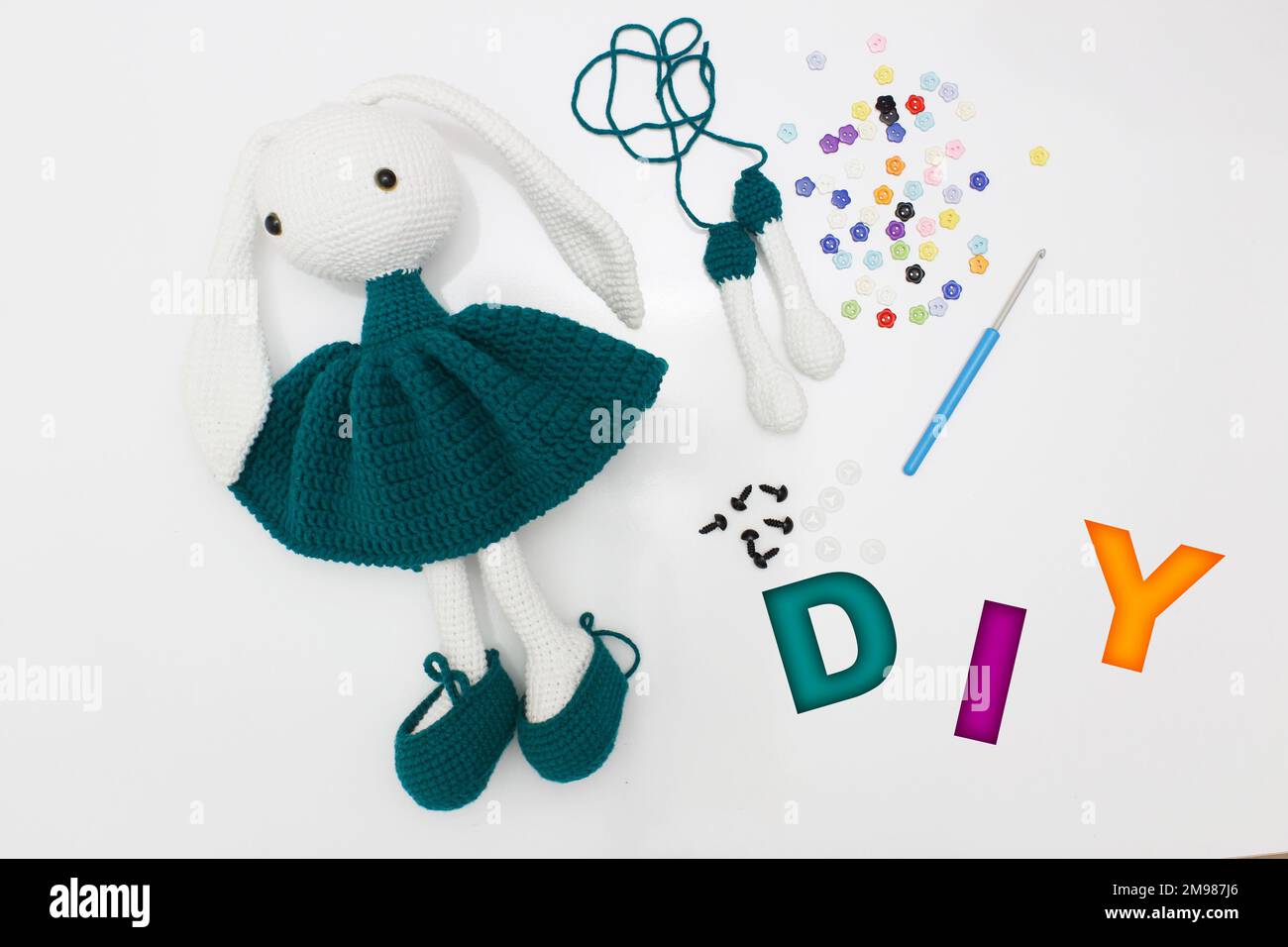 Konzeptidee „To it yourself“ (selbst machen). Gestricktes Hasenspielzeug mit langen Ohren, isoliert auf weißem Hintergrund. Draufsicht. Stockfoto