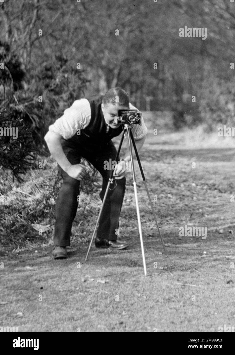 Ein Fotograf, der durch den Sucher seiner Kamera schaut, die auf einem Stativ steht. Stockfoto