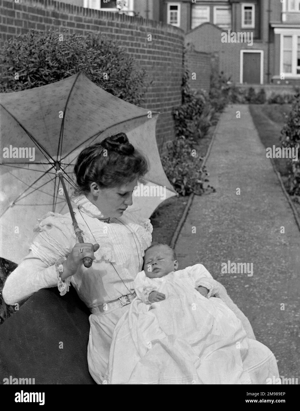 Mutter und Baby sitzen in einem Garten mit Sonnenschirm. Stockfoto