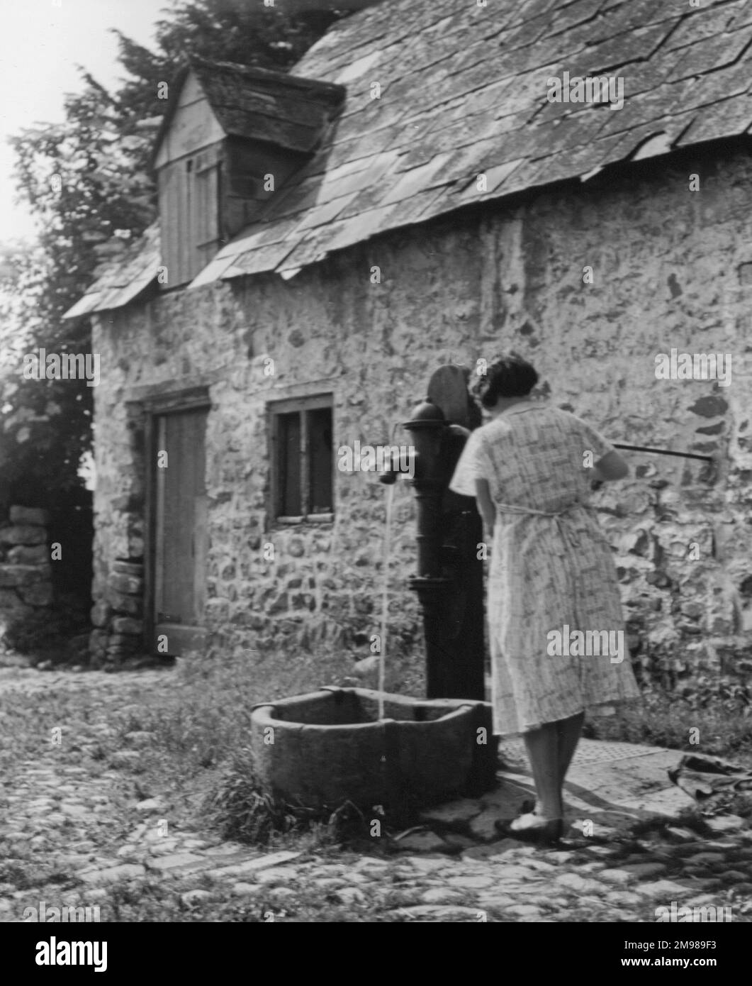 Eine Frau, die Wasser aus einer Dorfpumpe pumpt, England. Stockfoto