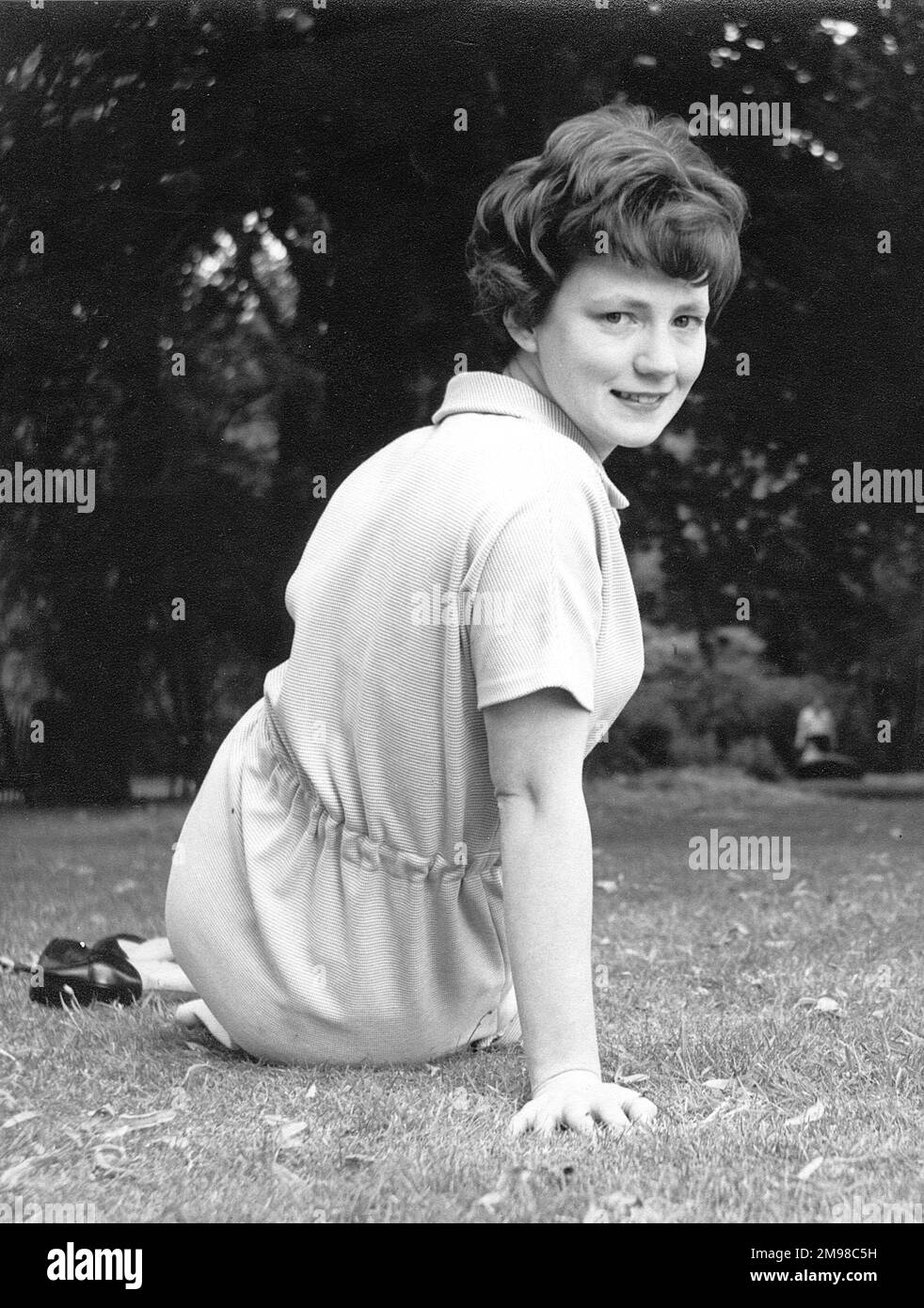Attraktive junge Dame, die auf dem Gras sitzt und in die Kamera lächelt. Stockfoto