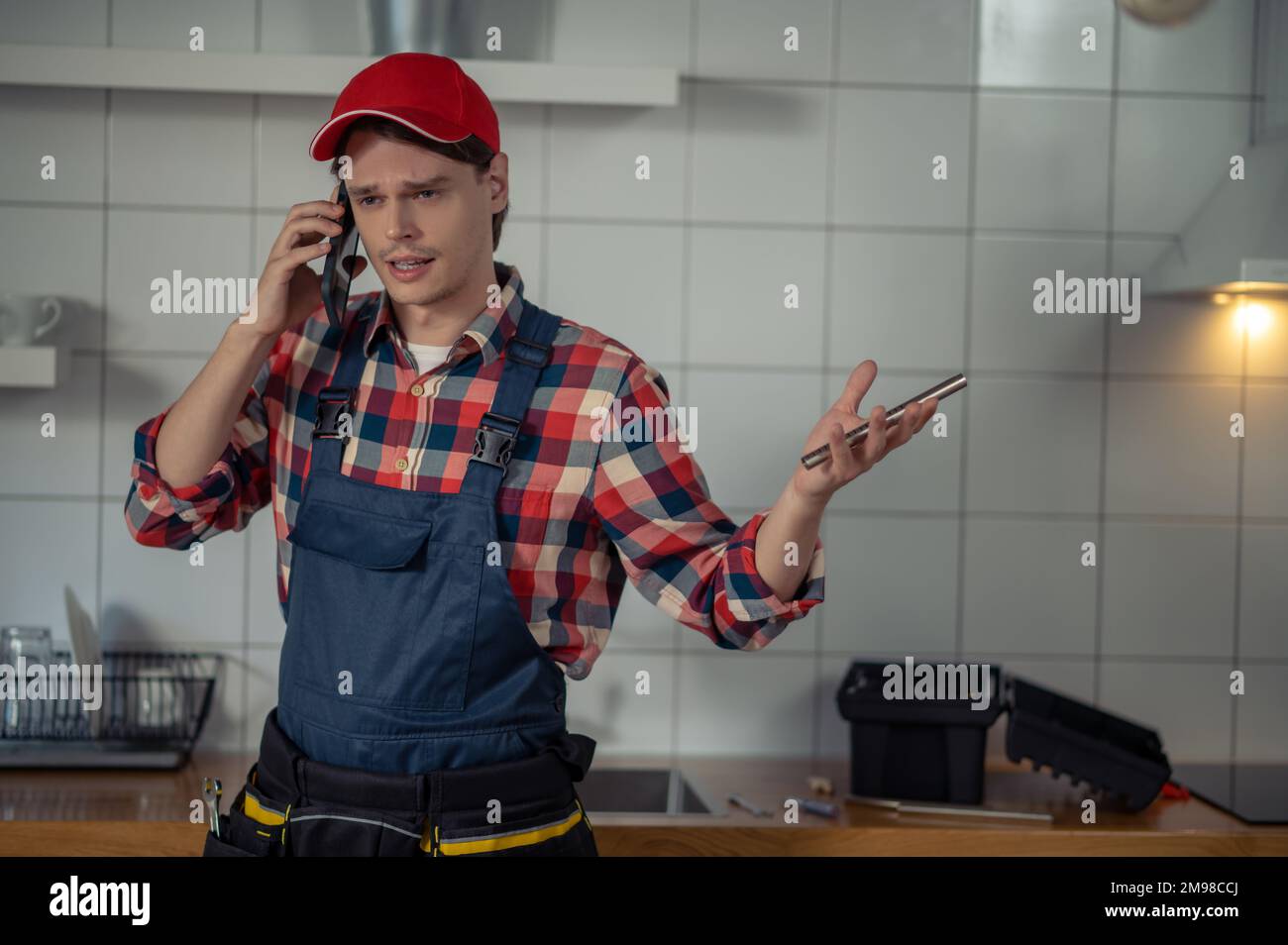 Taillenhochgezogenes Porträt eines ernsthaften Mechanikers, der etwas auf dem Handy in der Kundenküche diskutiert Stockfoto