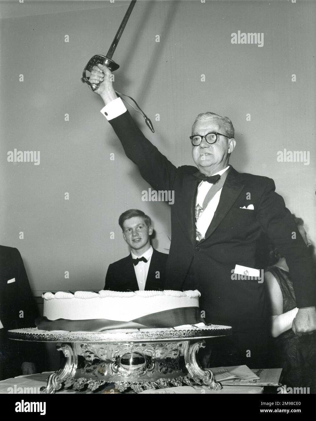 Sir George Gardner, Präsident von Raes 1965-1966, bereitet sich darauf vor, den hundertjährigen Geburtstagskuchen mit dem zeremoniellen Schwert von Brigadegeneral Sir Osborne Mance, dem langjährigen Mitglied der Gesellschaft, auf dem Centenary Conversazione, der am 12. Januar 1966 im Wissenschaftsmuseum stattfand, zu schneiden. Stockfoto