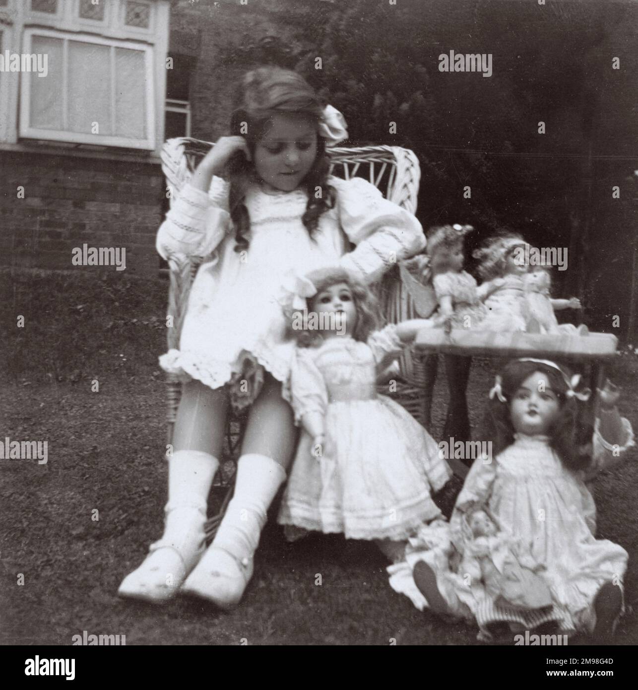 Kleines Mädchen (Violet Auerbach) mit ihren Puppen in einem Garten. Stockfoto