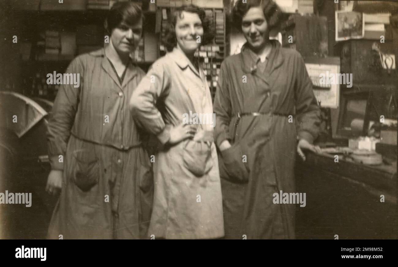 Drei Frauen in einem kleinen Unternehmen, die Overalls tragen, sind leider nicht leicht zu bestimmen, welchen Beruf sie genau haben. Die Maschine (hinten links) kann eine Form von Polierscheibe sein?? Stockfoto