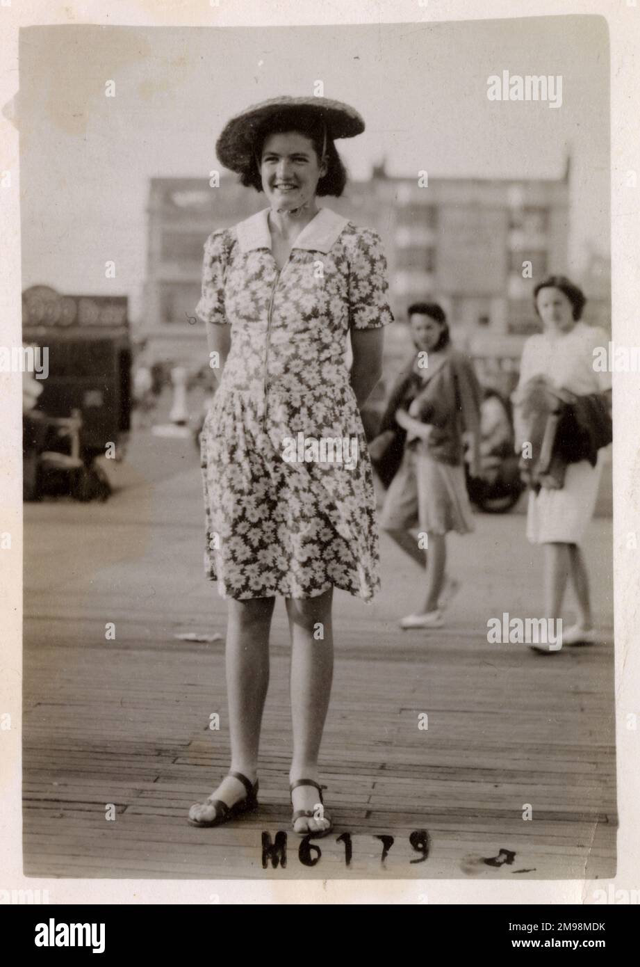 Junge Dame am Meer an einem recht luftigen Tag - sie trägt ein Kleid mit Blumenmuster und ihre Mütze benötigt sicherlich den Kinnriemen, um zu verhindern, dass er für immer weggeblasen wird... Stockfoto