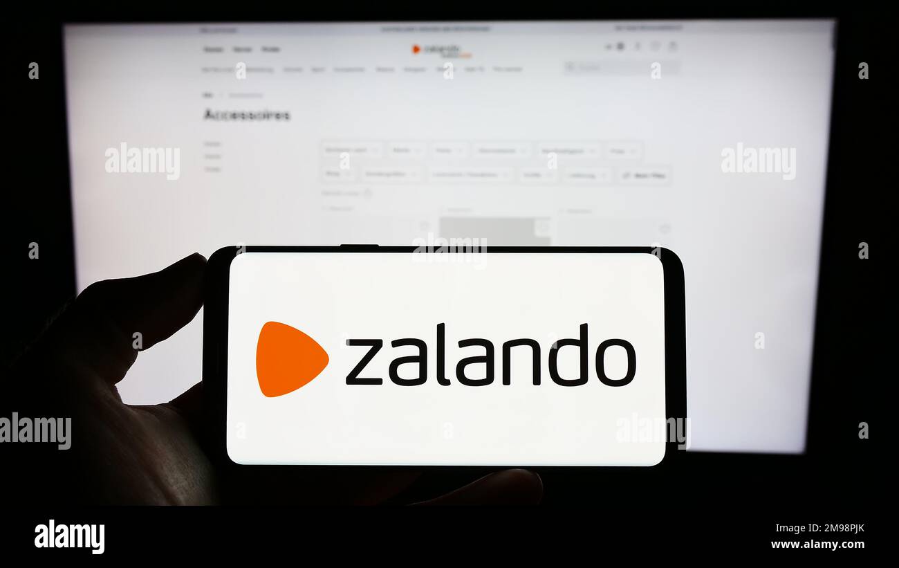 Person, die ein Mobiltelefon mit dem Logo des deutschen E-Commerce-Unternehmens Zalando SE auf dem Bildschirm vor der geschäftlichen Webseite hält. Konzentrieren Sie sich auf das Display des Telefons. Stockfoto
