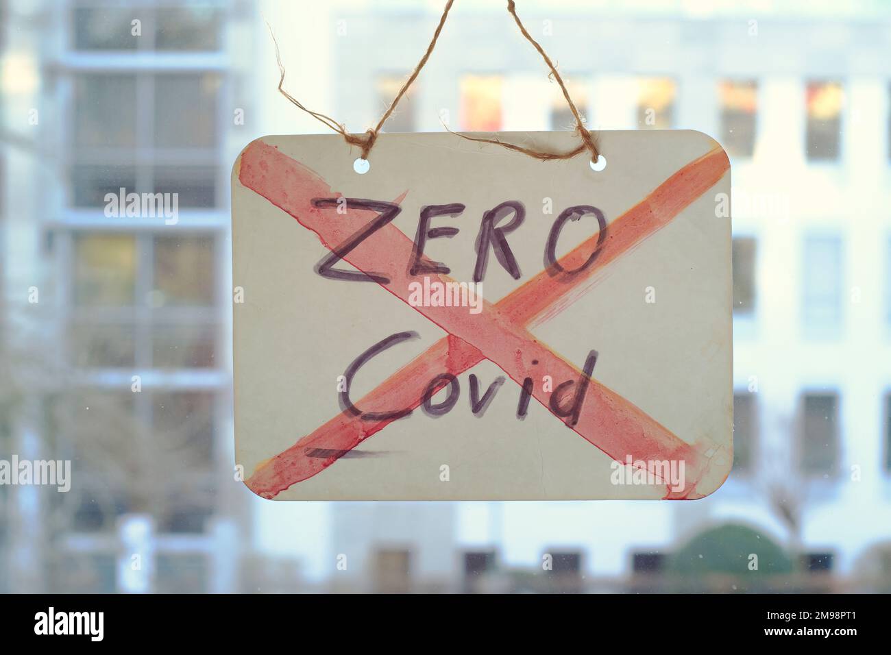 End Zero Covid-Schild am Fenster, Bürogebäude hinten Stockfoto