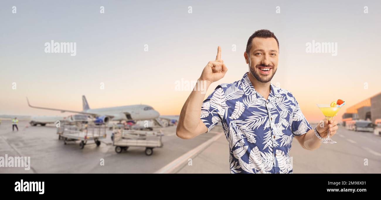 Ein junger Mann, der ein Glas Cocktail hält und auf den Flughafen zeigt Stockfoto