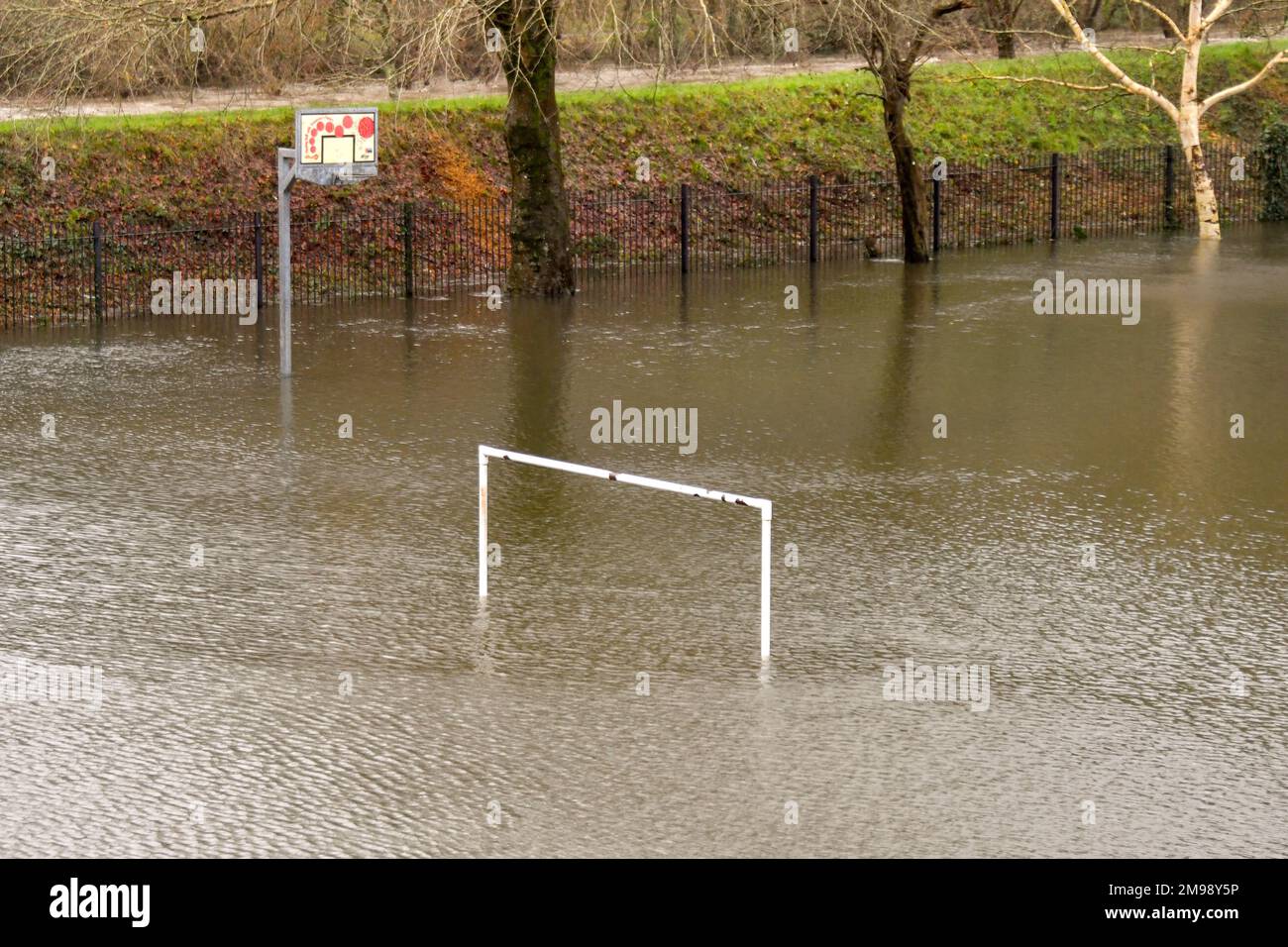 Weiße Torpfosten auf einem Fußballfeld und ein Korb auf einem Basketballfeld unter Wasser aufgrund von Überschwemmungen. Keine Menschen. Stockfoto