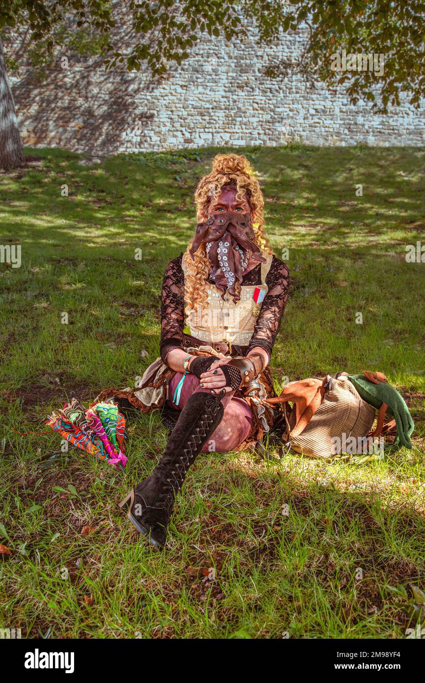 Eine merkwürdig aussehende weibliche Steampunk, die auf Gras sitzt, hat einen Tintenfisch an ihrem Gesicht. Stockfoto