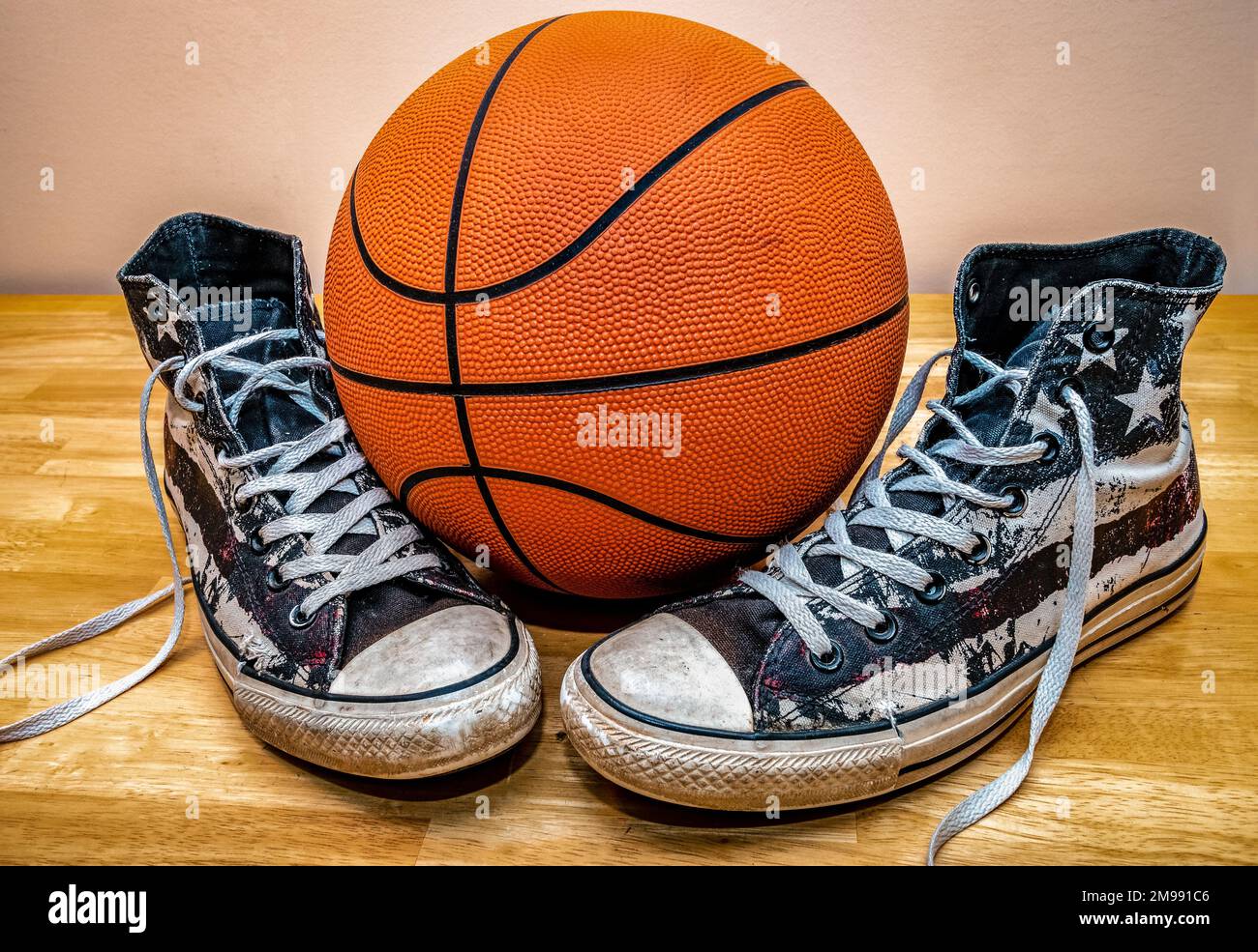 Basketball und ein Paar klassische Basketballschuhe aus Segeltuch auf Parkettboden. Stockfoto