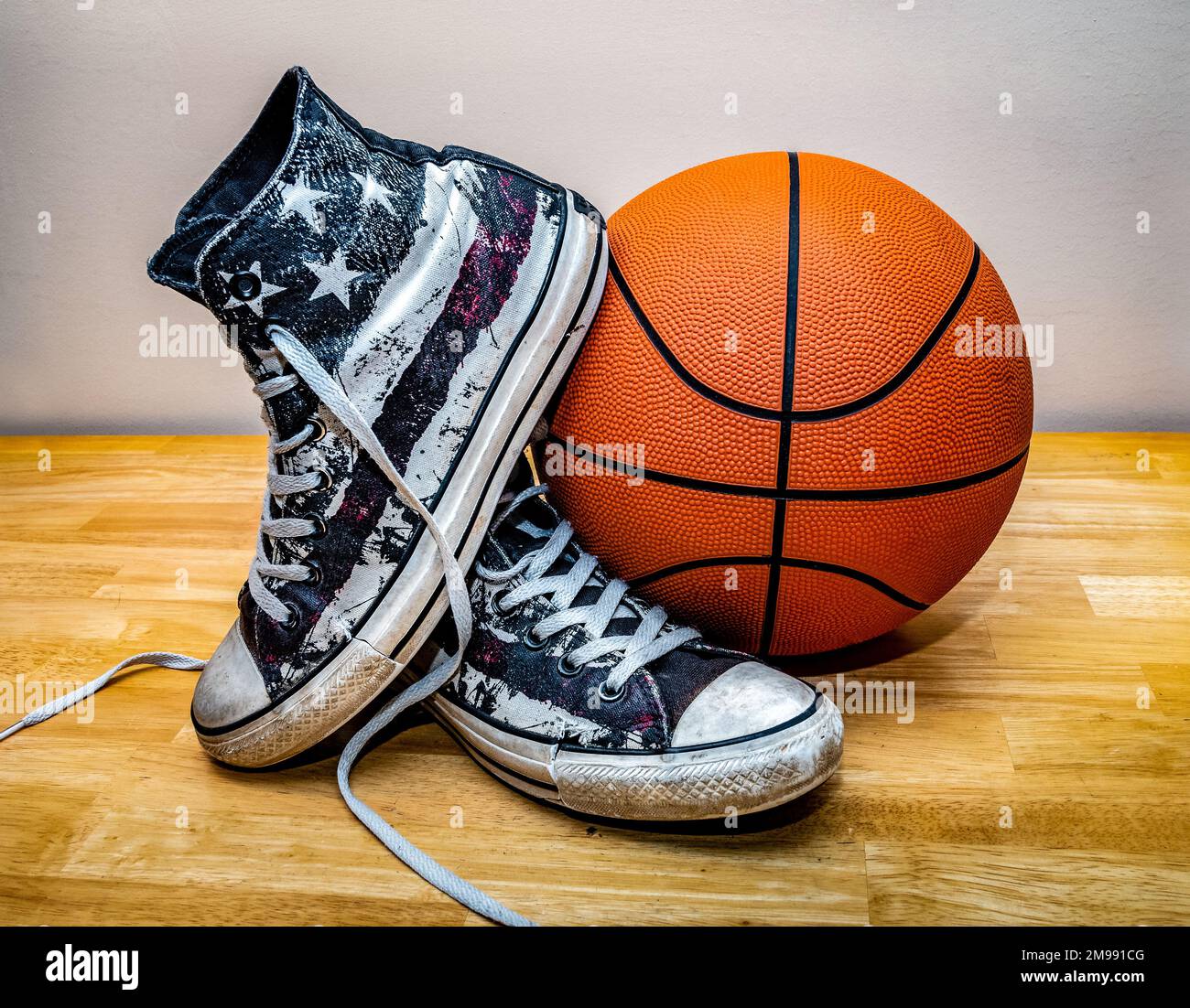 Basketball und ein Paar klassische Basketballschuhe aus Segeltuch auf Parkettboden. Stockfoto