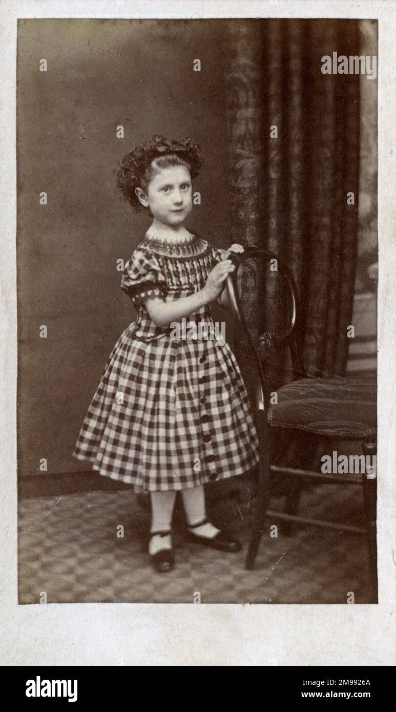 Studiofoto eines jungen Mädchens in einem karierten Kleid, ihr dunkles Locken-Haar teilweise zurückgebunden. Stockfoto