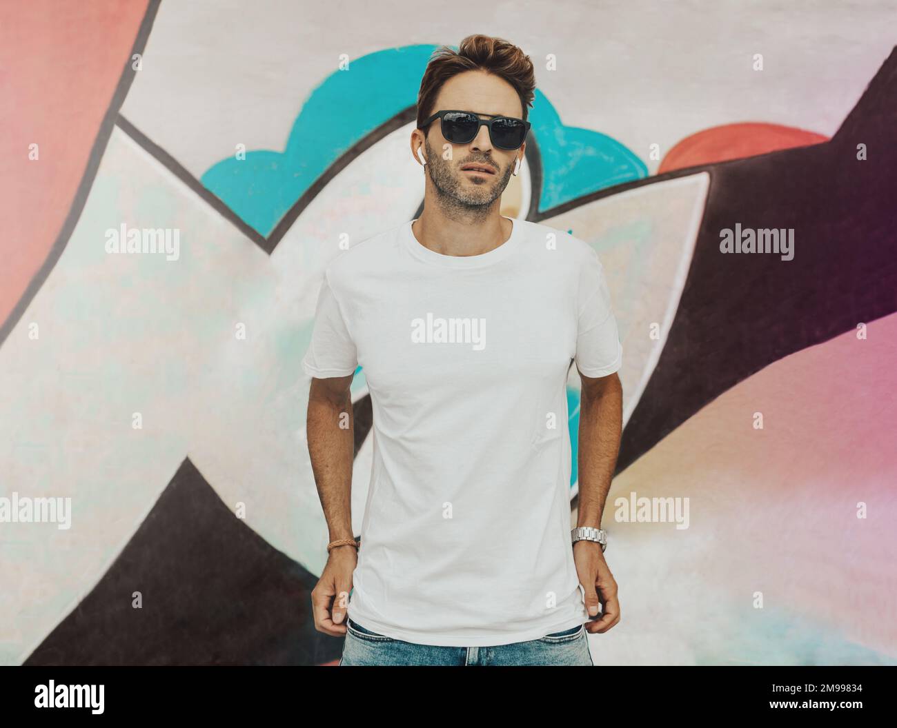 Der junge hübsche Kerl steht auf einem Graffiti-Wandhintergrund. Der Mann trägt ein weißes, leeres, einfaches T-Shirt ohne Logo. Stockfoto