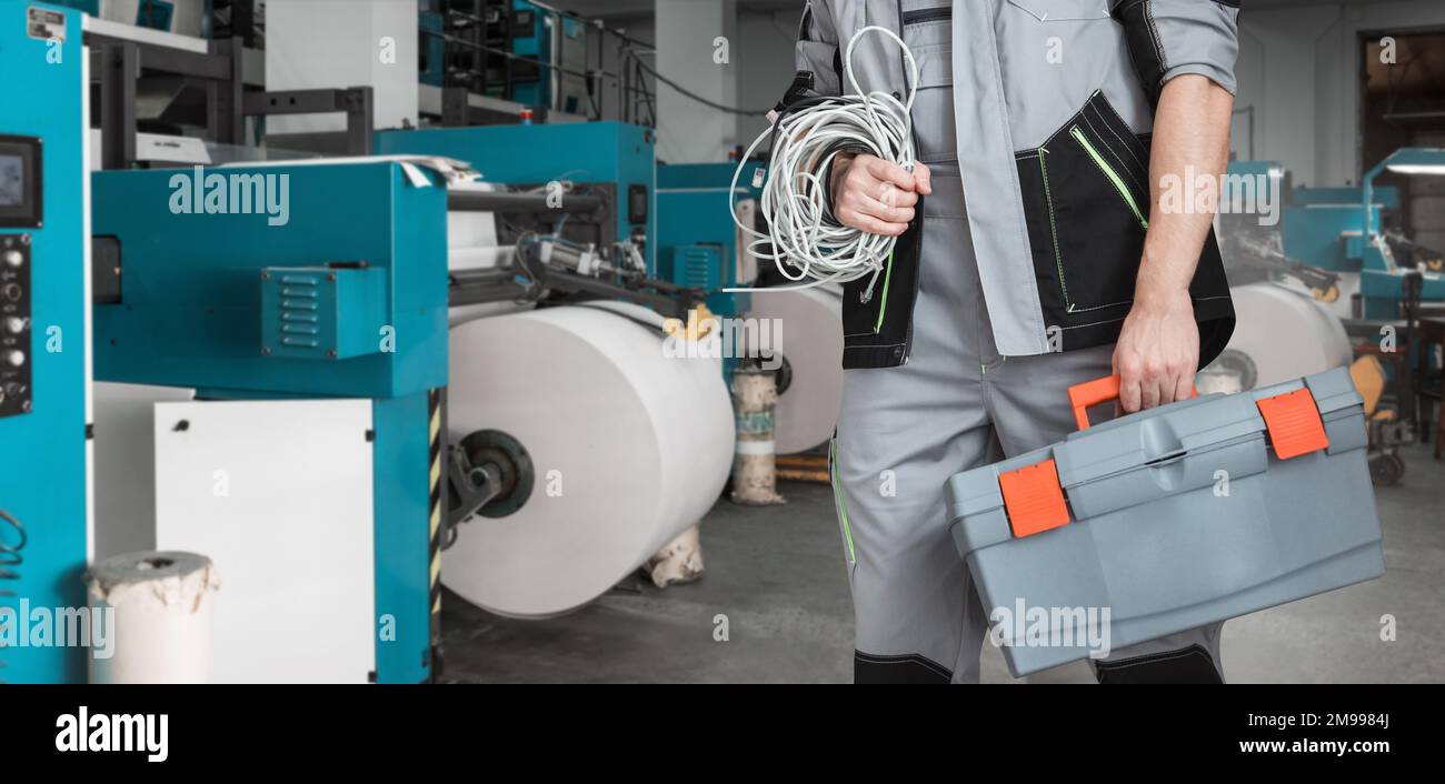 Mann mit Werkzeugkasten, der in einer Druckerei mit einer Druckmaschine arbeitet Stockfoto
