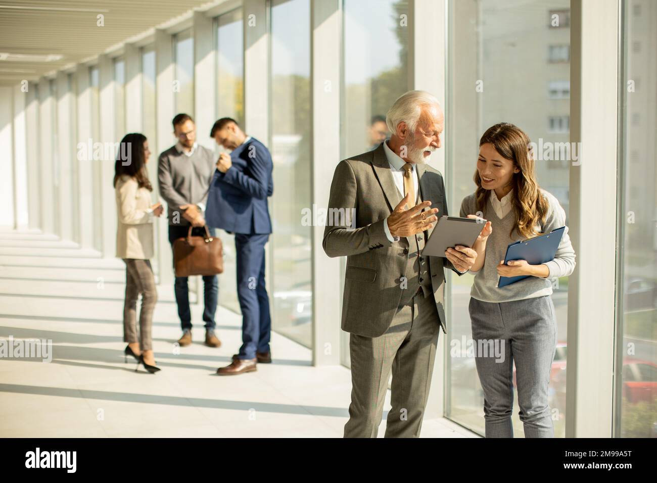 Attraktiver Geschäftsmann mit seiner jungen Frau Coleague, der im Büro ein digitales Tablet benutzt Stockfoto