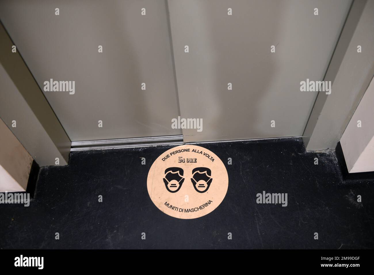 Schild, das angibt, dass auf dem Lift eine Maske getragen werden muss, wobei maximal zwei Personen gleichzeitig anwesend sein dürfen Stockfoto