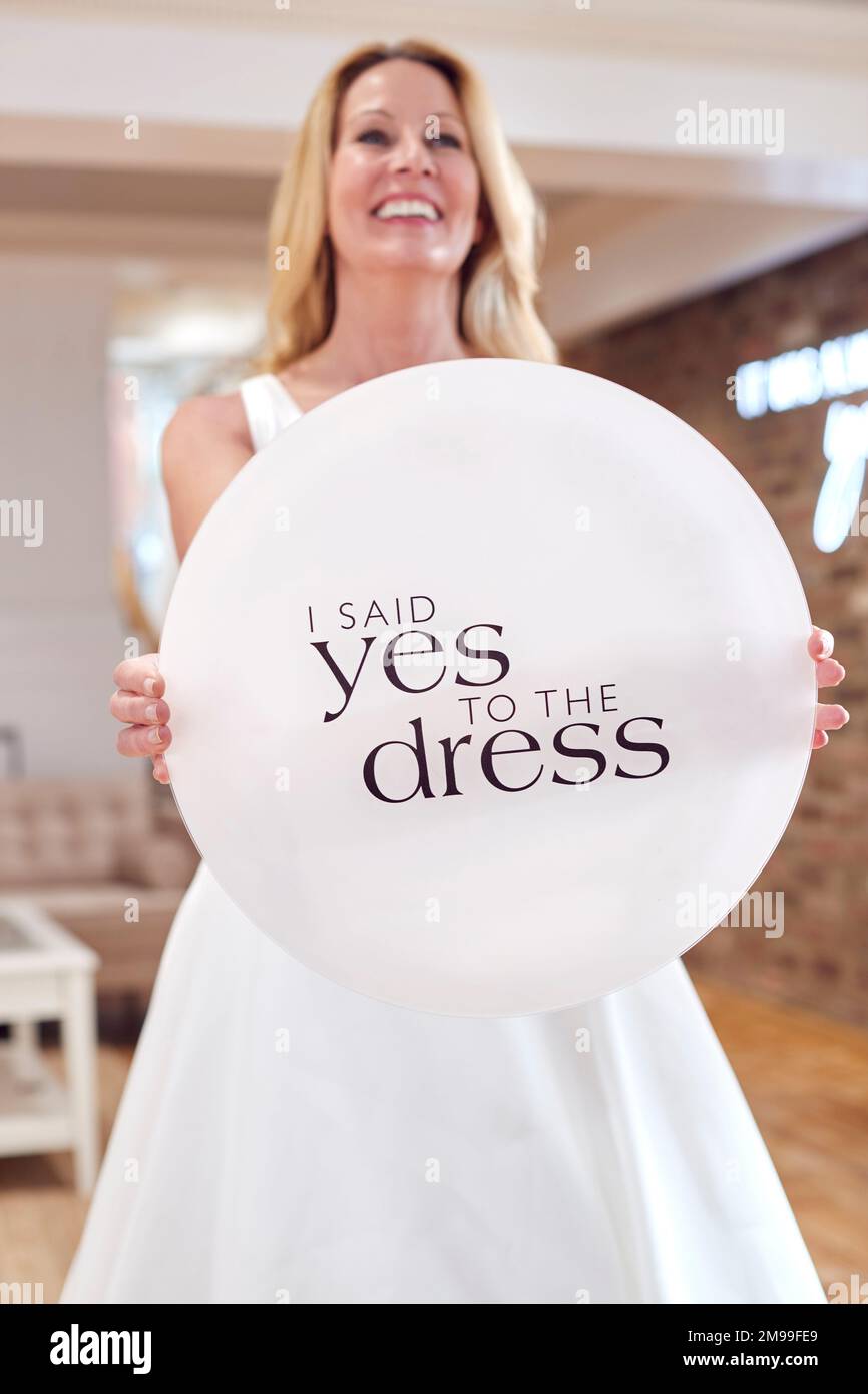 Smiling Mature Bride Planning Wedding In Bridal Store Mit Dem Schild „Yes To The Dress“ (Ja Zum Kleid) Stockfoto