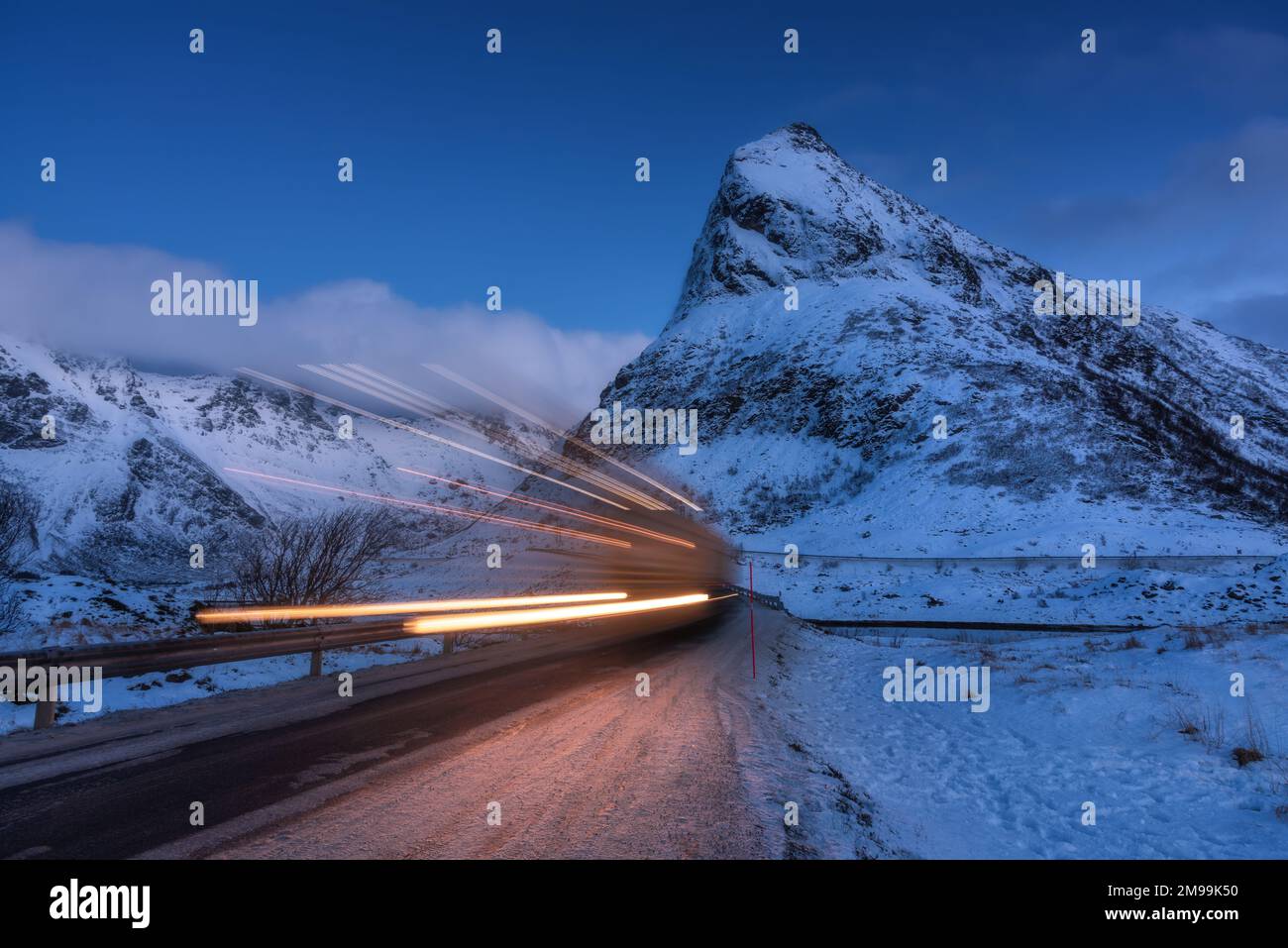Verschneite Berge und verschwommene Autoscheinwerfer im Winter auf der Straße Stockfoto