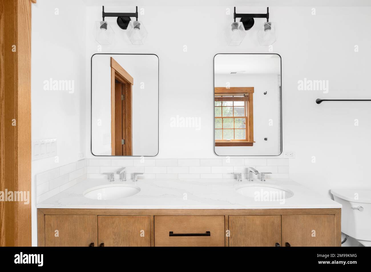 Ein wunderschönes Badezimmer mit Holzschrank, Marmorablagefläche, Subway-Farbspritzer und schwarzen Lichtern über den Spiegeln. Stockfoto