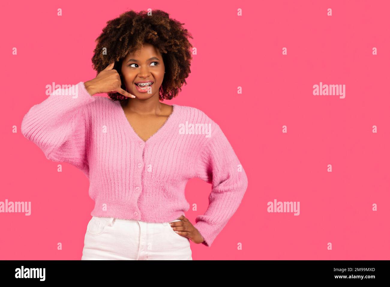 Fröhliche, hübsche, junge afroamerikanische, lockige Frau mit einer Zahnspange, die am imaginären Telefon anruft, viel Spaß beim Reden Stockfoto