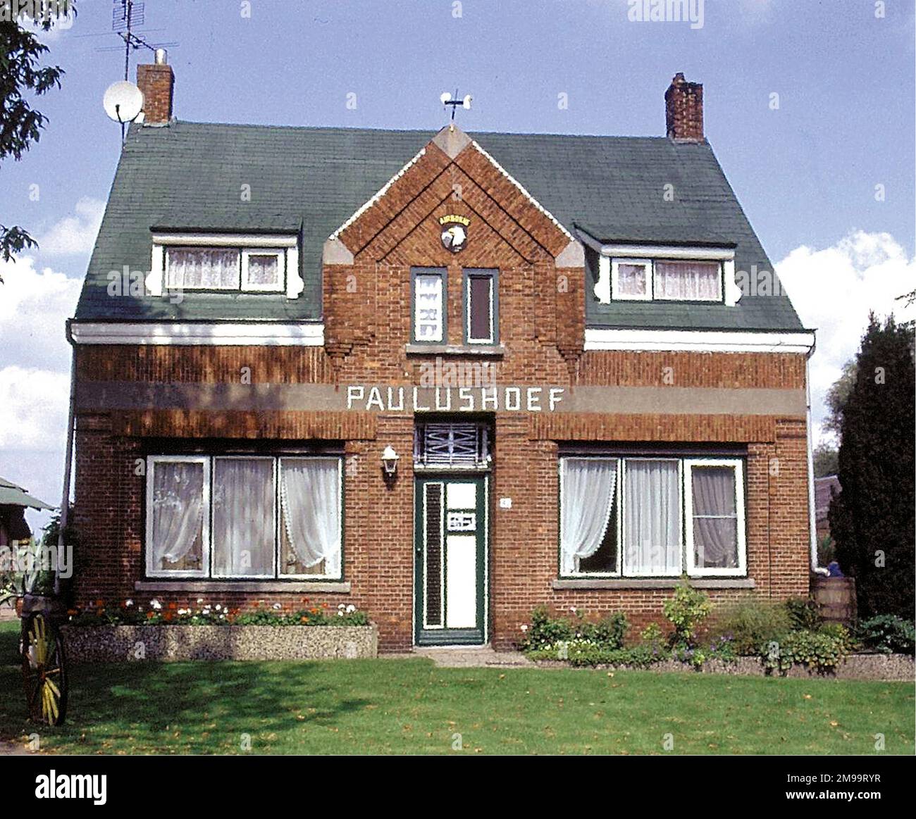 Der Besitzer dieser Farm, Wan van Overveld, hat einen Fallschirm aus Metall im Garten errichtet und auf dem Haus ist ein schreiender Adler. Letztere sollte den 40. Jahrestag der Operation Market Garden feiern und war ein Geschenk der Vereinigung der niederländischen Freunde der Luftfahrt. Am 17. 1944. September gab Liza van Overeld, Die damals 14 Jahre alt war, ihr Haus auf einer Farm in der Nähe mit ihrer Mutter und ihrer zwei Jahre alten Schwester verließ, um in die Kirche zu gehen. Während des Gottesdienstes erzählte der Priester ihnen, dass die Kirche von Deutschen umgeben war und dass sie nach Holländern suchten, die für sie Schützenlöcher entlang des Sohnes graben würden Stockfoto