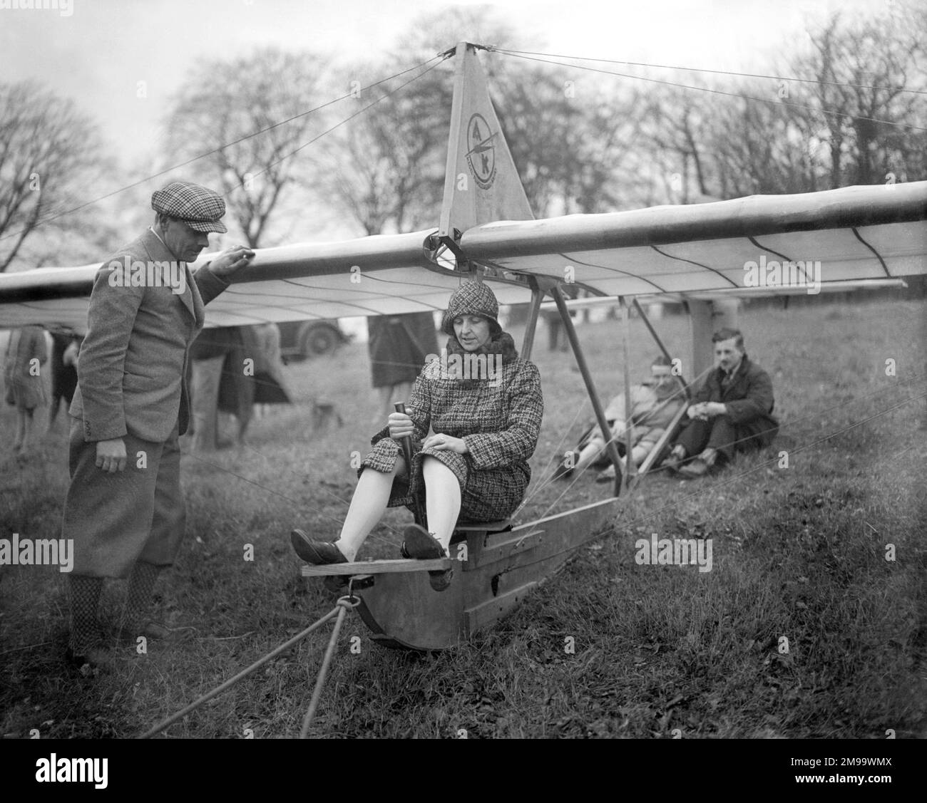 Dame Mary Bailey, Lady Bailey, DBE (nee Westenra) (1890-1960), irische Pilotin, versucht die Steuerung in Vorbereitung auf ihren Flug im Zogling-Hauptgleiter in der Nähe von Wendover in Buckinghamshire. Lady Bailey wurde die erste Frau, die einen Gleiter steuerte, kurz nachdem dieses Foto gemacht wurde. Im Vordergrund kann das Gummiband verwendet werden, um den anfänglichen Drang zu erzeugen, wobei die zurückhaltende Crew unter der Heckebene sitzt, um den Gleiter zurückzuhalten, bis ausreichend Spannung auf den Gummizug ausgeübt wird. Der Zogling wurde in Deutschland vom „Kegel-Flugzeugbau Kassel“ mit dem unverwechselbaren Firmenlogo o gebaut Stockfoto