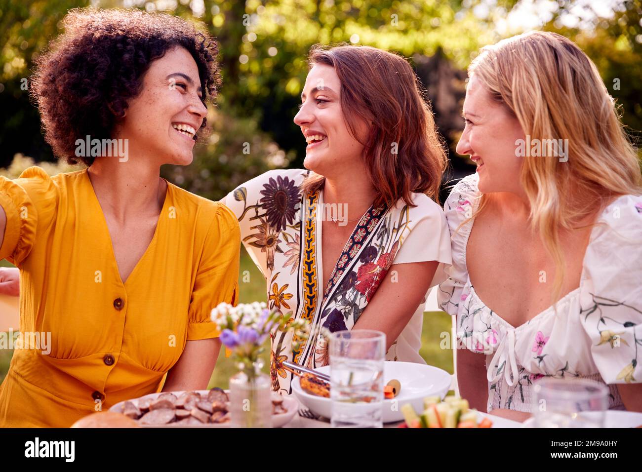 Drei Weibliche Freunde Sitzen Draußen Im Summer Garden At Home Und Essen Zusammen Stockfoto