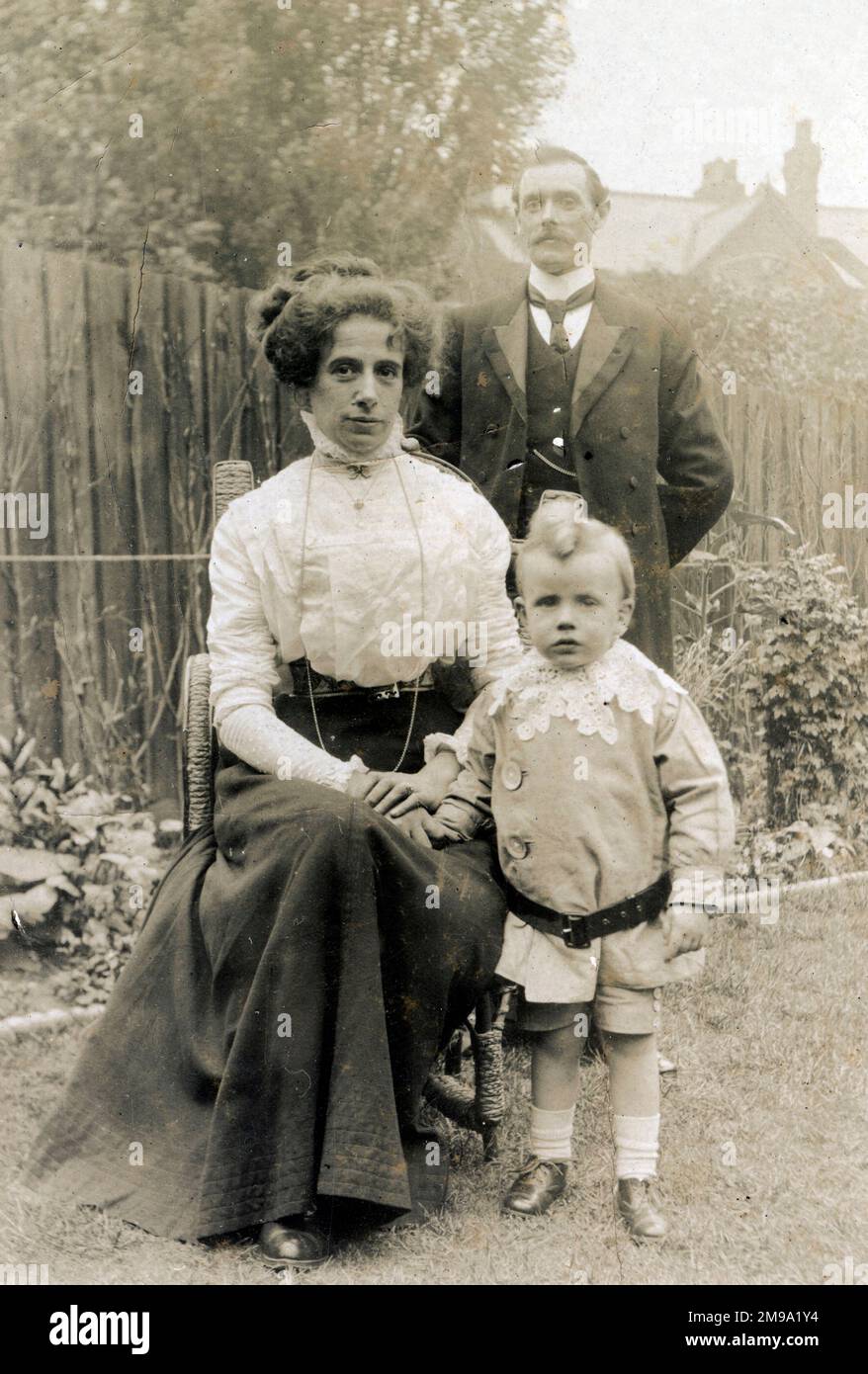 Familie im Garten – der kleine Junge trägt ein bemerkenswertes Kostüm und hat einen noch bemerkenswerteren Haarschnitt! Stockfoto