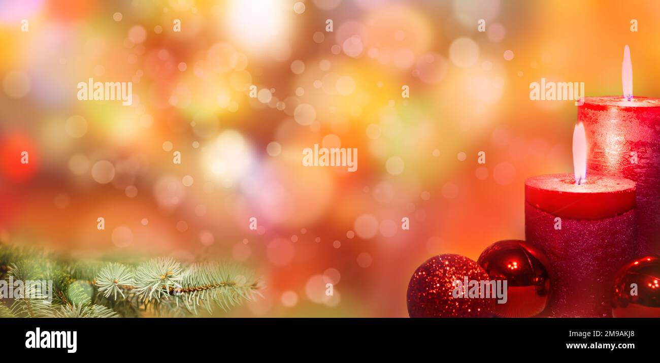 Brennende Weihnachtskerzen mit roten Kugeln und silbernen Fichtenzweigen mit abstrakten Unschärfe-Lichtern. Stockfoto