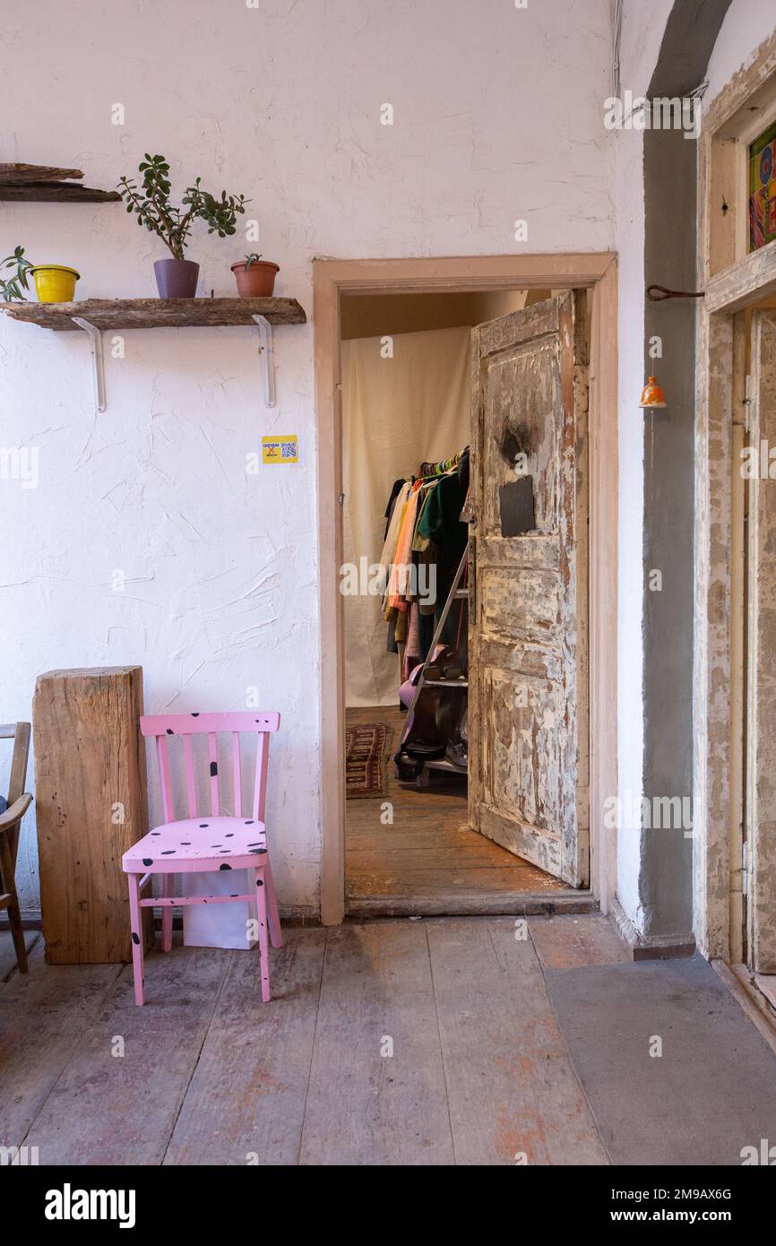 Ein kleiner, versteckter Gebrauchtwarenladen mit pinkfarbenen Stühlen, Pflanzen, Regalen, einem Kleiderschrank und weißen Wänden Stockfoto
